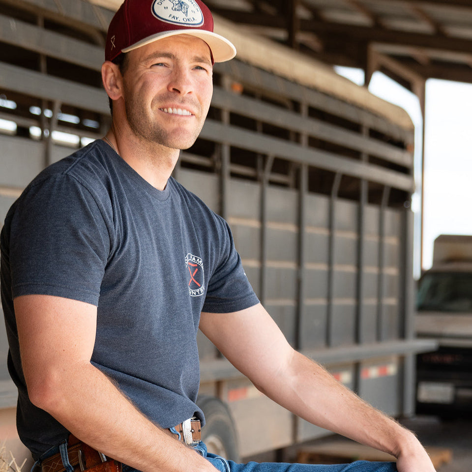 Gatlin Didier, Durango Team member and Western Influencer, sitting at his farm on a stack of straw in front of a livestock trailer.