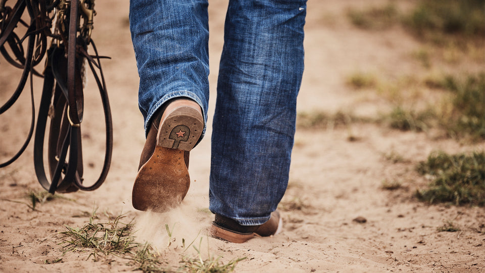 Outsole view of a cowboy walking on a dirt road.