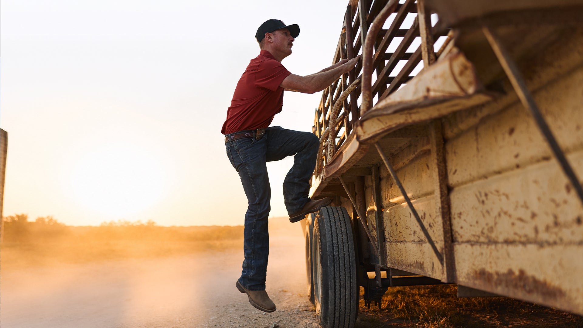 Man climbing onto a large wooden trailer at sunseT wearing Durango boots