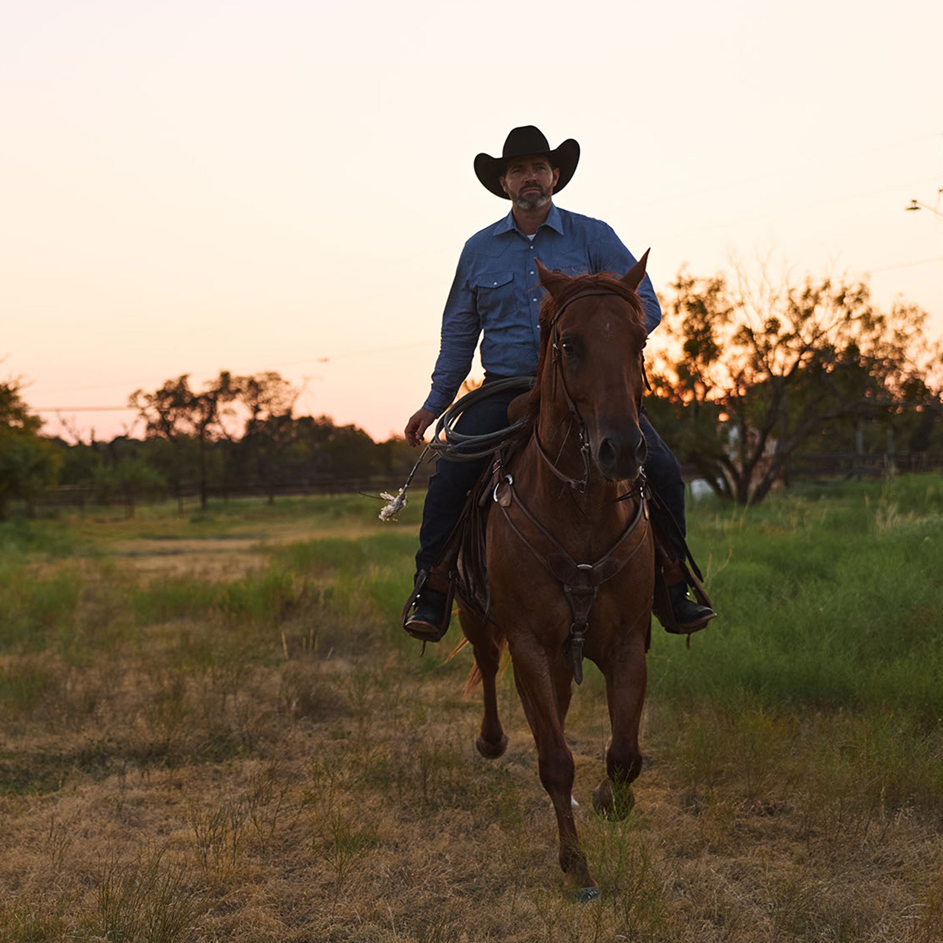 Man riding a horse in a field during sunset wearing durango boots