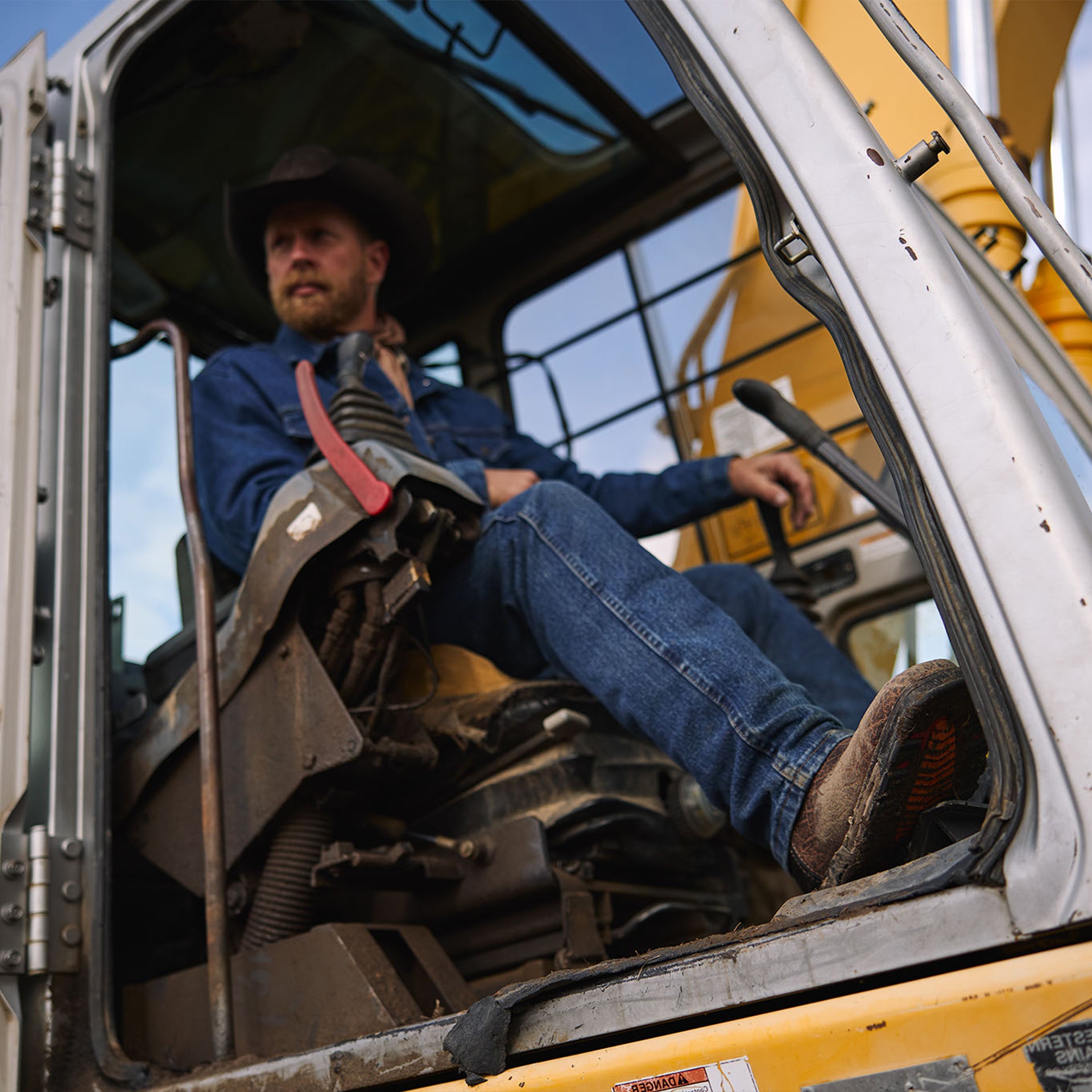 Man sitting inside a large piece of construction equipment on a clear day wearing durango work boots
