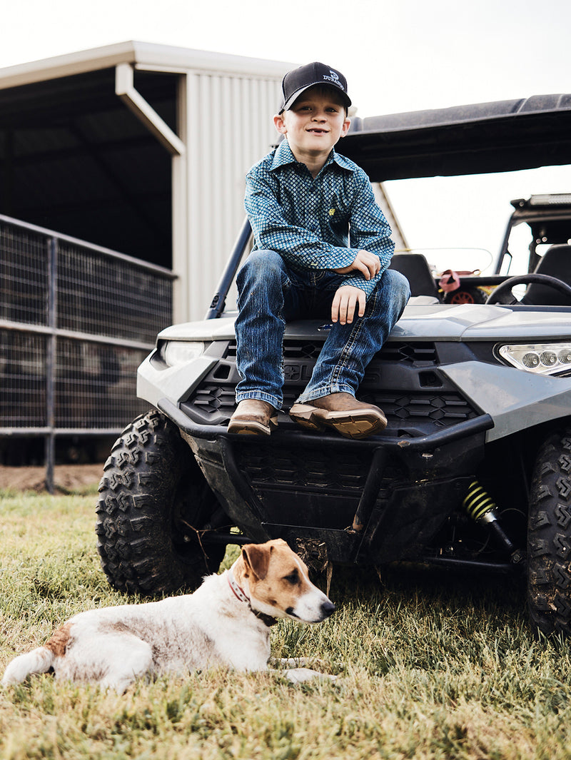 Child sitting on an ATV with a dog nearby, outdoors.
