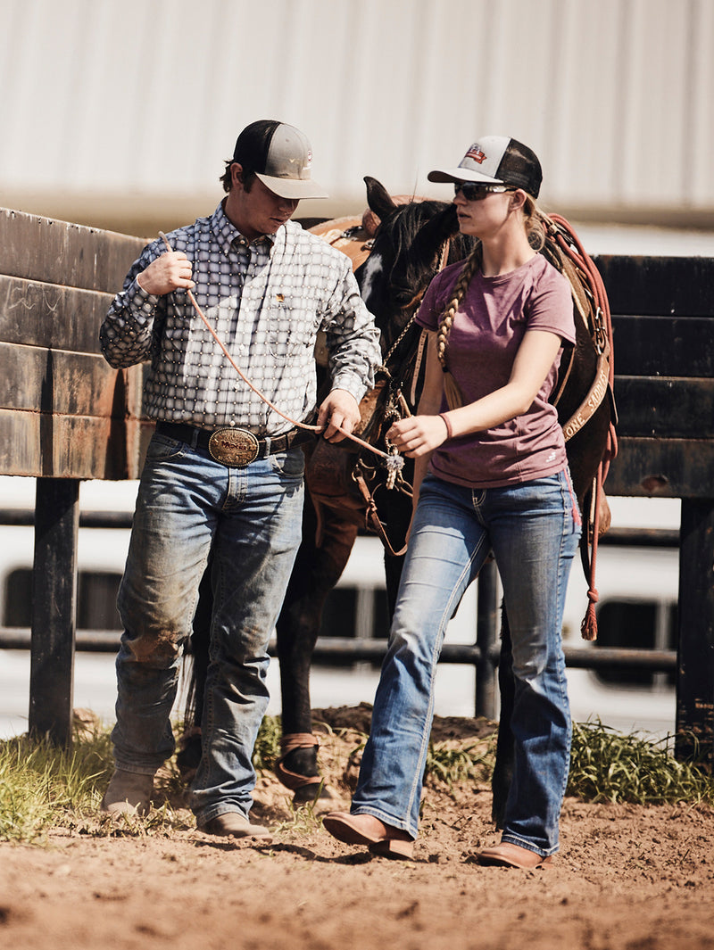Two people preparing a horse for riding in an outdoor setting.
