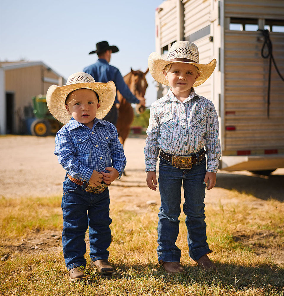 Brother and sister standing in the grass in front of a horse trailer