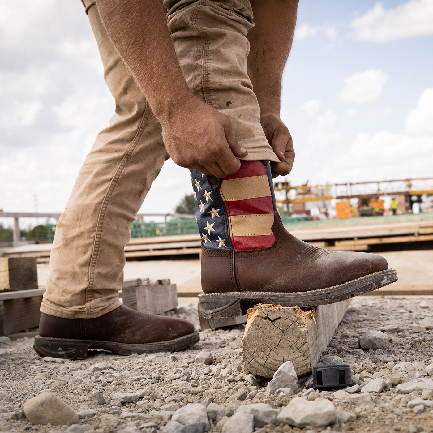 Person wearing a western work boot with an American flag design on a construction site.
